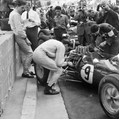 Aux essais à Monaco, Jim aide à changer les bougies de la Lotus 25 sous l'oeil amusé de Trevor Taylor
